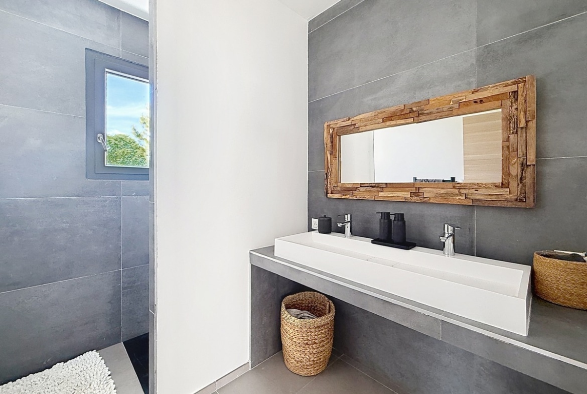 Salle de bains avec carrelage grand format gris anthracite et douche à l'italienne ouverte. Vasque blanche rectangulaire double robinetterie et miroir encadré bois recyclé.