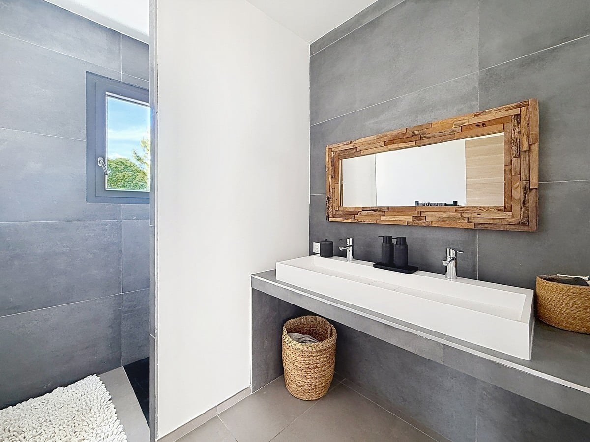 Salle de bains avec carrelage grand format gris anthracite et douche à l'italienne ouverte. Vasque blanche rectangulaire double robinetterie et miroir encadré bois recyclé.