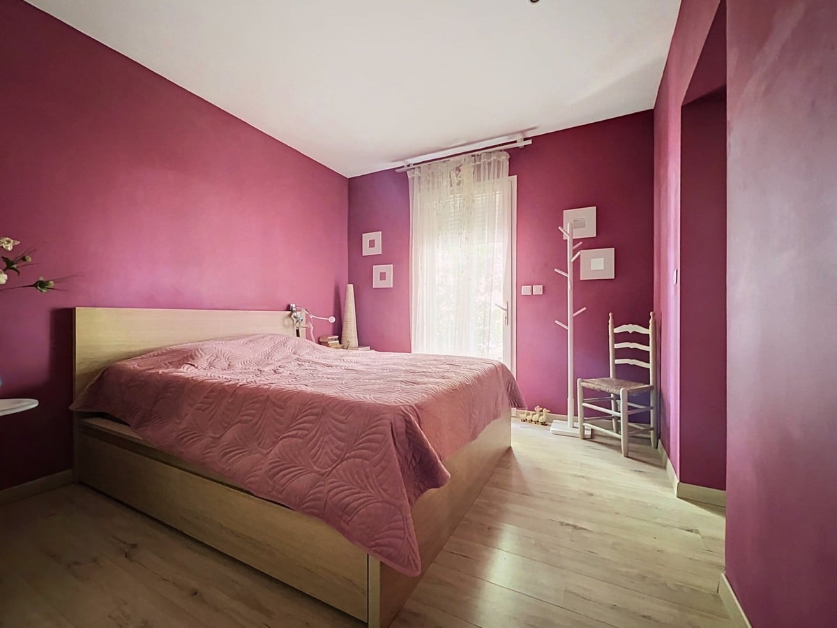 Chambre avec murs peints en rose fuchsia et parquet clair en bois. Lit double avec cadre en bois naturel, couvre-lit rose pâle à motifs de feuilles, chaise traditionnelle blanche et porte-manteau blanc en forme d'arbre.