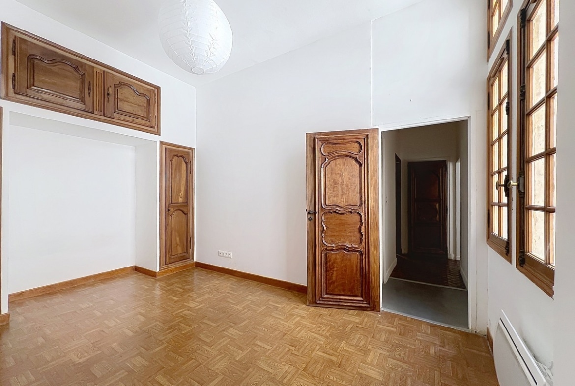 Chambre aux murs blancs avec boiseries en chêne d'époque, portes à panneaux sculptés et placards hauts encadrés de moulures. Sol en parquet point de Hongrie et fenêtre à petits carreaux en bois sur le côté droit.