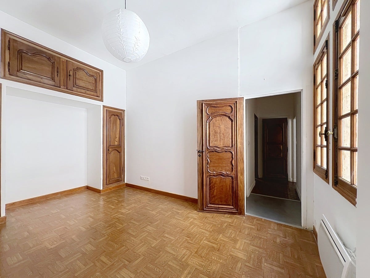 Chambre aux murs blancs avec boiseries en chêne d'époque, portes à panneaux sculptés et placards hauts encadrés de moulures. Sol en parquet point de Hongrie et fenêtre à petits carreaux en bois sur le côté droit.