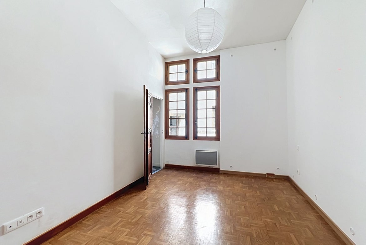 Chambre vide aux murs blancs avec double fenêtre à petits carreaux sous imposte, encadrée de bois. Sol en parquet point de Hongrie et suspension sphérique en papier blanc au plafond.