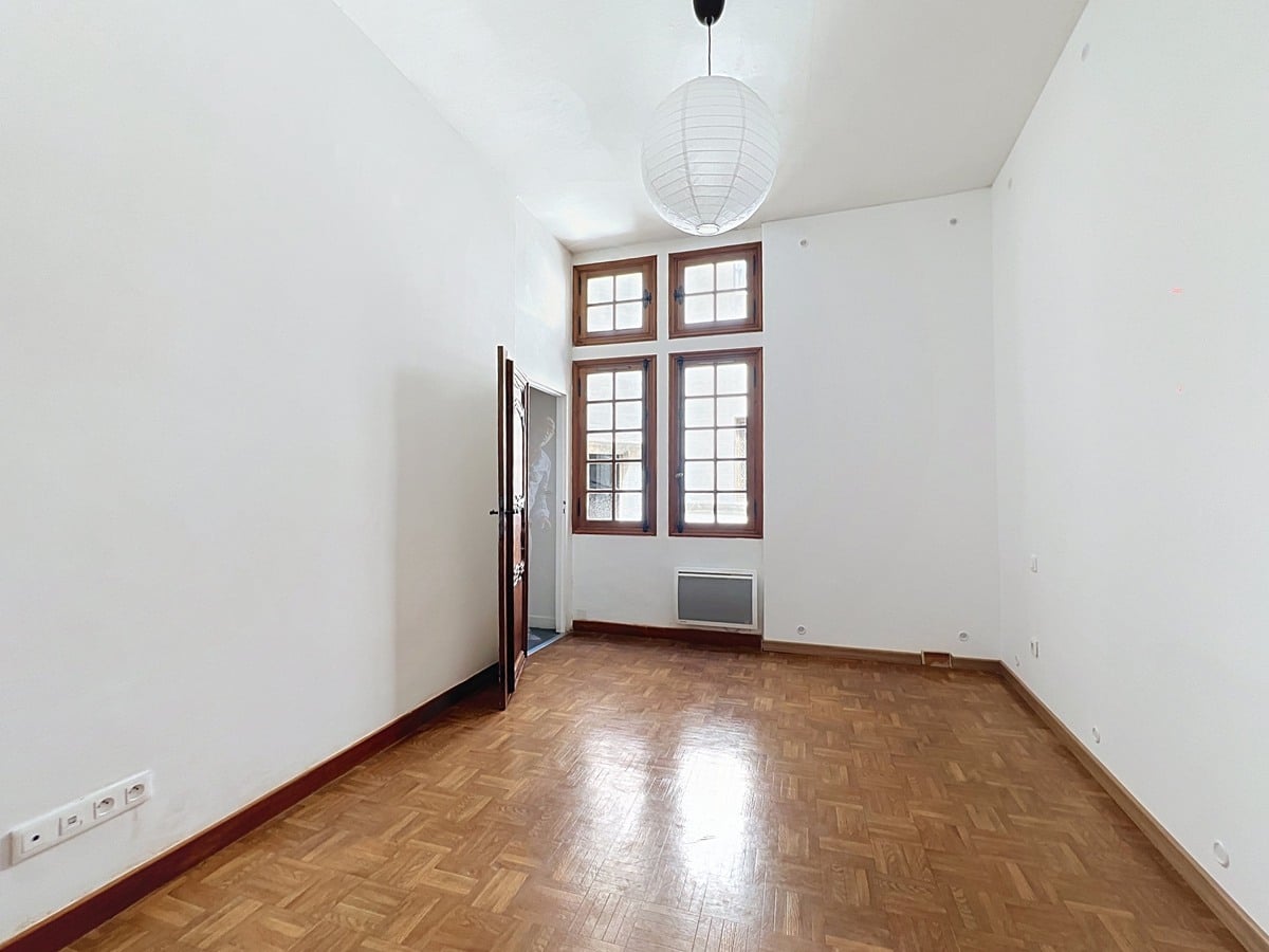 Chambre vide aux murs blancs avec double fenêtre à petits carreaux sous imposte, encadrée de bois. Sol en parquet point de Hongrie et suspension sphérique en papier blanc au plafond.