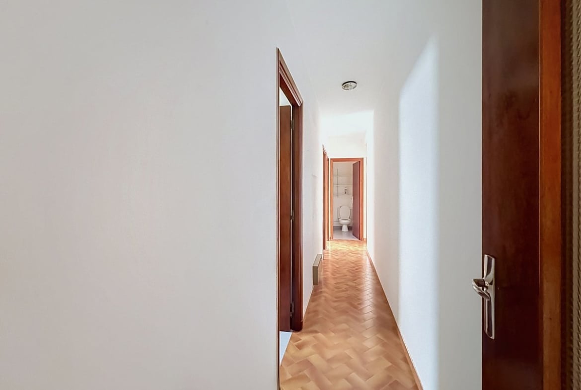 Couloir étroit aux murs blancs avec un sol en parquet bois clair posé en point de Hongrie, desservant plusieurs pièces avec des portes en bois foncé. En fond de couloir, une porte ouverte laisse apparaître un WC blanc.