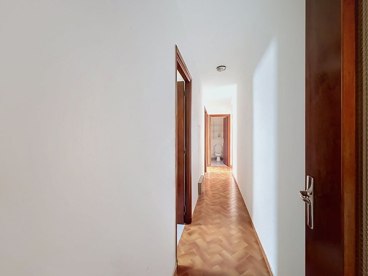 Couloir étroit aux murs blancs avec un sol en parquet bois clair posé en point de Hongrie, desservant plusieurs pièces avec des portes en bois foncé. En fond de couloir, une porte ouverte laisse apparaître un WC blanc.
