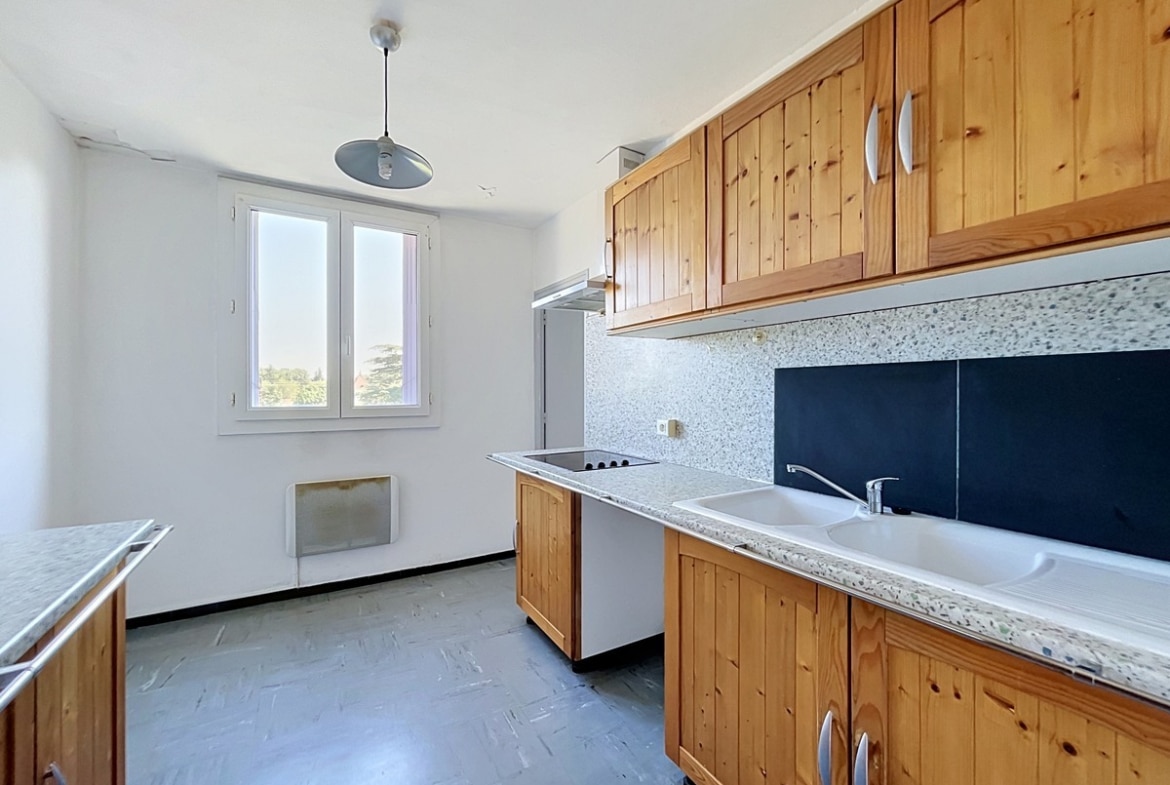 Cuisine séparée avec meubles hauts et bas en bois pin massif, plan de travail en granit terrazzo gris et double évier blanc encastré. Une plaque de cuisson vitrocéramique est intégrée au plan de travail central, un réfrigérateur blanc est visible en fond de cuisine, et une fenêtre à double battant apporte la lumière naturelle. Le sol est recouvert d'un carrelage vinyle gris à motif géométrique. Photo 5 — terrasse-appartement-avignon-vente-p5-web.jpg 🔗 Slug / Nom de fichier balcon-vue-appartement-avignon-vente 📌 Title Balcon avec vue dégagée d'un appartement en vente à Avignon 🏷️ Balise Alt Balcon filant en béton brut avec garde-corps métallique noir, situé en étage élevé avec vue sur un ensemble de bâtiments résidentiels modernes en enduit blanc et brique orangée. Un caisson de volet roulant en métal bleu-violet est visible à gauche, et un terrain en friche apparaît au pied de l'immeuble. Le ciel est entièrement dégagé, sans nuages. Photo 6 — salle-de-bain-appartement-avignon-vente-p6-web.jpg 🔗 Slug / Nom de fichier salle-de-bain-appartement-avignon-vente 📌 Title Salle de bain avec baignoire d'un appartement en vente à Avignon 🏷️ Balise Alt Salle de bain carrelée du sol au plafond avec faïence beige rosé et frise décorative en losanges gris-bleu, équipée d'une baignoire encastrée avec pare-baignoire en verre coulissant à cadre aluminium. Un meuble vasque blanc avec miroir éclairé et rangements hauts est installé sur le mur de droite, et une petite fenêtre en hauteur assure la ventilation naturelle.