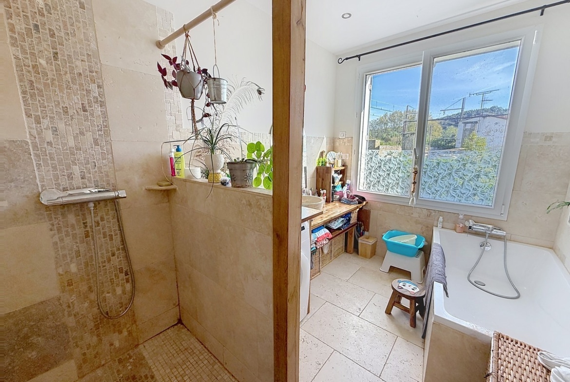 Salle de bain carrelée en pierre travertin beige, dotée d'une douche à l'italienne ouverte avec colonne de douche chromée et d'une baignoire encastrée blanche équipée d'un mitigeur mural. La pièce dispose d'une fenêtre à double vitrage avec film décoratif, d'un plan vasque en bois et de plusieurs plantes vertes en suspension sur une barre en bois séparant la douche du reste de la pièce. Photo 7 — cuisine-appartement-avignon-vente-p7-web.jpg 🔗 Slug / Nom de fichier cuisine-sejour-appartement-vente-villeneuve-les-avignon 📌 Title Cuisine ouverte avec salle à manger d'un appartement en vente à Villeneuve-lès-Avignon 🏷️ Balise Alt Cuisine aménagée en bois clair avec plan de travail, lave-vaisselle en inox et cuisinière à gaz, ouverte sur une salle à manger avec grande table rectangulaire et chaises dépareillées. La pièce est éclairée par deux fenêtres dont une en arc de cercle avec rideaux bordeaux, et meublée d'un buffet et d'un vaisselier en bois patiné blanc. Photo 8 — sejour-appartement-avignon-vente-p8-web.jpg 🔗 Slug / Nom de fichier sejour-ouvert-appartement-vente-villeneuve-les-avignon 📌 Title Séjour ouvert sur cuisine d'un appartement en vente à Villeneuve-lès-Avignon 🏷️ Balise Alt Grande pièce de vie à plan ouvert avec sol en parquet stratifié clair, comprenant un salon avec canapé gris et table basse blanche ovale, communiquant directement avec la salle à manger et la cuisine en arrière-plan. Un lustre en métal forgé noir et une fenêtre cintrée avec rideau bordeaux apportent du caractère à la pièce lumineuse aux murs blancs. Photo 9 — sejour-appartement-avignon-vente-p9-web.jpg 🔗 Slug / Nom de fichier salon-poele-appartement-vente-villeneuve-les-avignon 📌 Title Salon avec poêle à bois d'un appartement en vente à Villeneuve-lès-Avignon 🏷️ Balise Alt Salon aux murs blancs avec sol en parquet stratifié clair, équipé d'un poêle à bois en fonte noire avec conduit apparent et d'un canapé en cuir marron foncé. La pièce est meublée de plusieurs sièges dont un fauteuil rouge et un fauteuil rotin, avec un lustre en métal forgé rouge en suspension au plafond et des ouvertures vers un couloir avec escalier visible en arrière-plan. 📣
