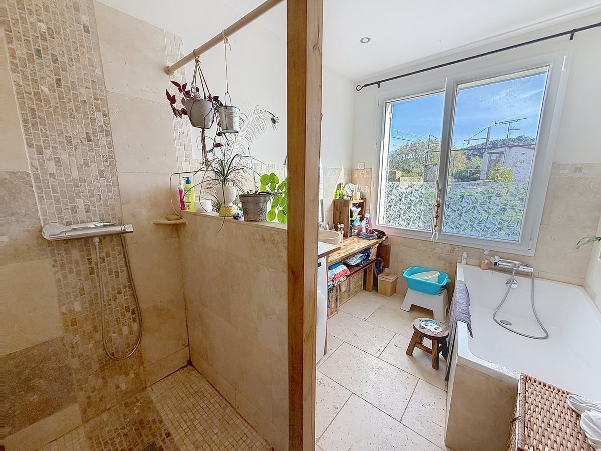 Salle de bain carrelée en pierre travertin beige, dotée d'une douche à l'italienne ouverte avec colonne de douche chromée et d'une baignoire encastrée blanche équipée d'un mitigeur mural. La pièce dispose d'une fenêtre à double vitrage avec film décoratif, d'un plan vasque en bois et de plusieurs plantes vertes en suspension sur une barre en bois séparant la douche du reste de la pièce. Photo 7 — cuisine-appartement-avignon-vente-p7-web.jpg 🔗 Slug / Nom de fichier cuisine-sejour-appartement-vente-villeneuve-les-avignon 📌 Title Cuisine ouverte avec salle à manger d'un appartement en vente à Villeneuve-lès-Avignon 🏷️ Balise Alt Cuisine aménagée en bois clair avec plan de travail, lave-vaisselle en inox et cuisinière à gaz, ouverte sur une salle à manger avec grande table rectangulaire et chaises dépareillées. La pièce est éclairée par deux fenêtres dont une en arc de cercle avec rideaux bordeaux, et meublée d'un buffet et d'un vaisselier en bois patiné blanc. Photo 8 — sejour-appartement-avignon-vente-p8-web.jpg 🔗 Slug / Nom de fichier sejour-ouvert-appartement-vente-villeneuve-les-avignon 📌 Title Séjour ouvert sur cuisine d'un appartement en vente à Villeneuve-lès-Avignon 🏷️ Balise Alt Grande pièce de vie à plan ouvert avec sol en parquet stratifié clair, comprenant un salon avec canapé gris et table basse blanche ovale, communiquant directement avec la salle à manger et la cuisine en arrière-plan. Un lustre en métal forgé noir et une fenêtre cintrée avec rideau bordeaux apportent du caractère à la pièce lumineuse aux murs blancs. Photo 9 — sejour-appartement-avignon-vente-p9-web.jpg 🔗 Slug / Nom de fichier salon-poele-appartement-vente-villeneuve-les-avignon 📌 Title Salon avec poêle à bois d'un appartement en vente à Villeneuve-lès-Avignon 🏷️ Balise Alt Salon aux murs blancs avec sol en parquet stratifié clair, équipé d'un poêle à bois en fonte noire avec conduit apparent et d'un canapé en cuir marron foncé. La pièce est meublée de plusieurs sièges dont un fauteuil rouge et un fauteuil rotin, avec un lustre en métal forgé rouge en suspension au plafond et des ouvertures vers un couloir avec escalier visible en arrière-plan. 📣