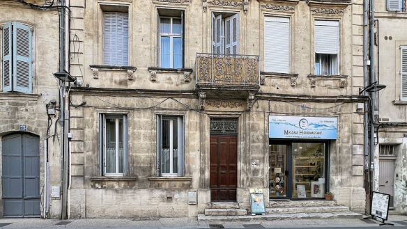 Façade haussmannienne en pierre de taille calcaire avec moulures sculptées, balcon en fer forgé ouvragé au premier étage et porte cochère en bois sombre à double vantail. Au rez-de-chaussée côté droit, devanture commerciale d'un salon de massage hydromassant avec vitrine et présentoirs visibles, numéro de rue 75 visible sur le pilastre gauche.
