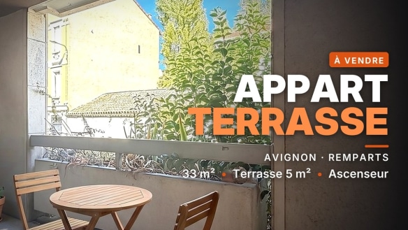 Terrasse de l'appartement T1 en vente à Avignon avec table ronde et deux chaises en bois, ouverte sur végétation et toitures voisines.