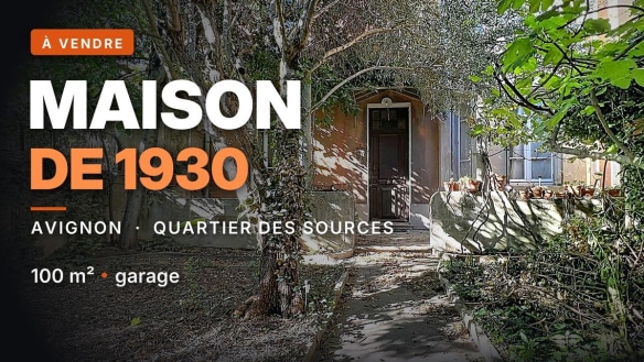 Façade en brique et enduit d'une maison des années 1930 avec porte d'entrée cintrée, partiellement dissimulée par une végétation dense composée d'arbres et arbustes. Allée en béton menant à l'entrée, entourée de branches et de feuillages envahissants, témoignant d'un jardin non entretenu nécessitant des travaux de remise en état.
