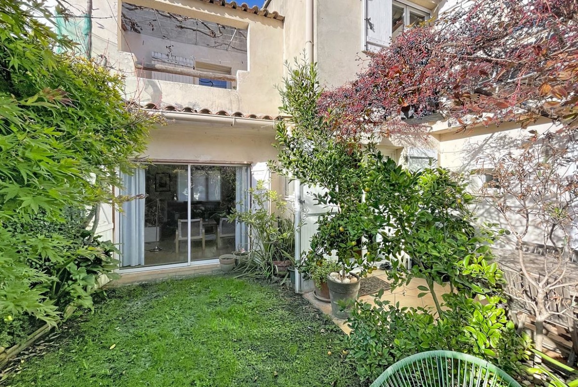 Jardin clos avec pelouse verte, terrasse carrelée beige et porte-fenêtre coulissante donnant sur le séjour, entouré d'arbustes et d'un citronnier en pot.