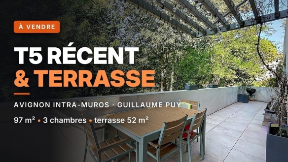 Terrasse dallée de carrelage gris clair équipée d'une table et chaises de jardin en aluminium gris et bois, couverte d'une pergola métallique noire avec guirlande lumineuse. La terrasse est bordée d'un muret blanc bas et donne sur une végétation dense d'arbres à feuilles vertes en arrière-plan.